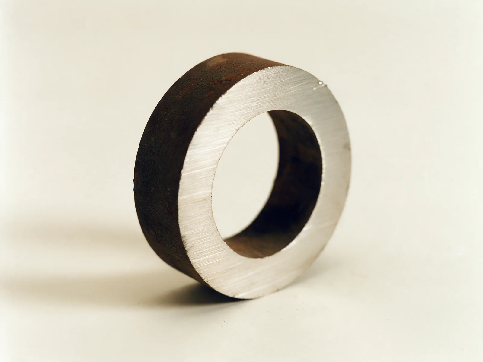 A cut ring from a retired reformer tube standing on edge: dark oxide scale outside, bright nickel-chromium alloy on the cut face